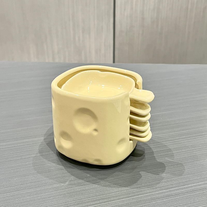 Stacked ceramic measuring cups in a cheese block design on a gray surface