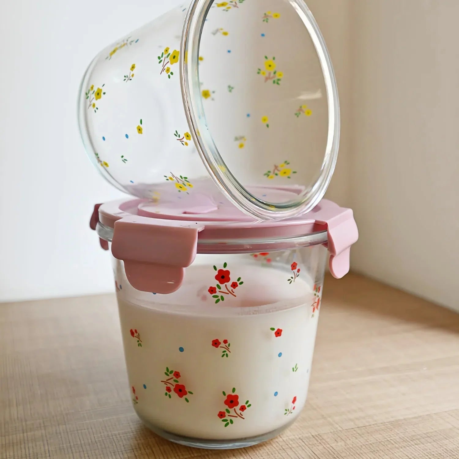 Glass food containers with floral print and pink lids on wooden table