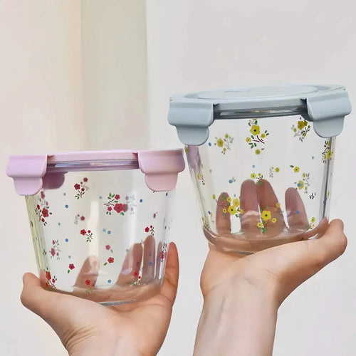 Two clear glass food storage containers with floral patterns and pastel lids held in hands