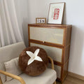 Minimalist living room with a round brown plush pillow, wooden rattan cabinet, and framed art