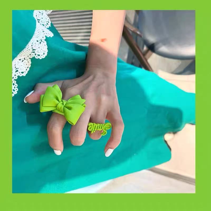 Green bow statement ring and smile ring worn on a hand